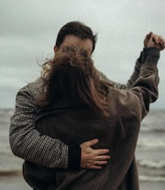 a man with long hair is holding his arms in the air while standing near the ocean