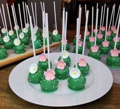 green cake pops with pink and white flowers on them sitting on a plate next to other desserts