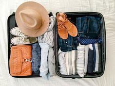 an open suitcase filled with clothes and shoes on top of a bed next to a white sheet