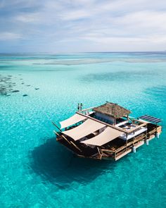 a boat floating in the middle of clear blue ocean water with people standing on it