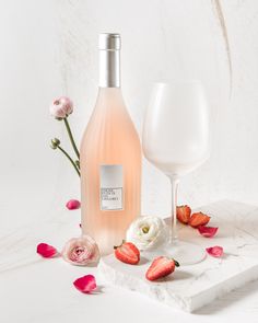 a bottle of wine next to a glass with strawberries and roses on the table