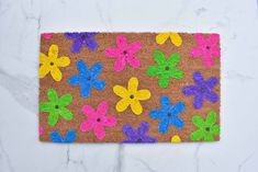 a door mat decorated with colorful flowers on a white marble countertop and blue, yellow, pink, green, purple, orange and black