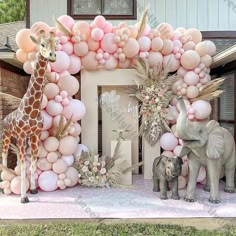 an elephant and giraffe stand in front of a balloon arch