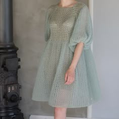 a woman standing in front of a stove wearing a light green dress and white shoes