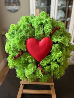 a green wreath with a red heart in the center on a wooden easel next to a window