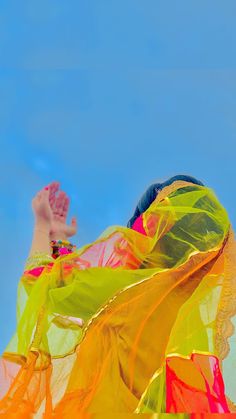 a woman with her hands up in the air while wearing a colorful dress and veil