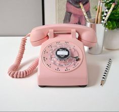 a pink phone sitting on top of a desk next to a pen and pencils