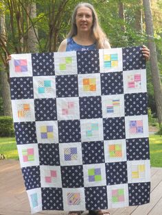 a woman holding up a quilt made from squares