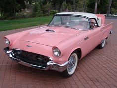 an old pink and white car is parked on the street