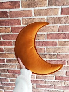 a person holding up a crescent shaped pillow in front of a brick wall with the moon on it