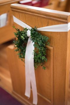 a wreath tied to the back of a wooden church pew with white ribbon around it