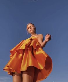 a woman in an orange dress flying through the air with a kite above her head