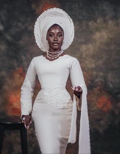 a woman in a white dress and headdress standing next to a black chair