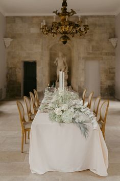 a table with white flowers and candles on it in front of a chandelier