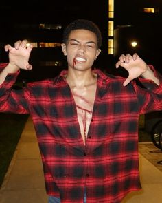 a young man with his hands in the air and wearing a red plaid shirt, standing on a sidewalk at night