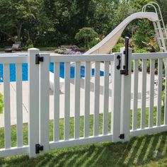 a white fence with a slide in the back ground and a swimming pool behind it