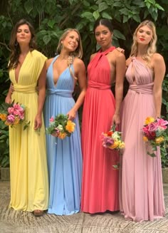 four beautiful women standing next to each other wearing different colored dresses and holding bouquets