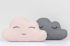 two pillows with eyes and eyelashes on them sitting next to each other in the shape of clouds