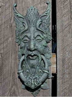 a metal door knockle with a face on it's side and a wooden fence in the background