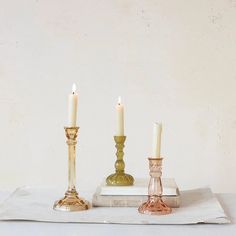 three candles sitting on top of a table next to a book and glass candle holder