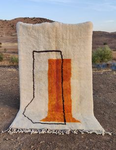 an orange and white rug sitting on top of a dirt field