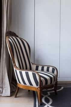 a black and white striped chair sitting in front of a window next to a curtain