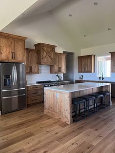 a large kitchen with wooden cabinets and stainless steel appliances in the center, along with two bar stools