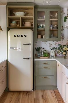 an old fashioned refrigerator is in the middle of a kitchen with wooden floors and green cabinets