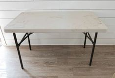 a white table sitting on top of a hard wood floor next to a brick wall