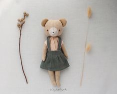 a teddy bear is sitting next to a dried flower and a needle - point doll