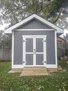 a small gray and white shed sitting in the grass