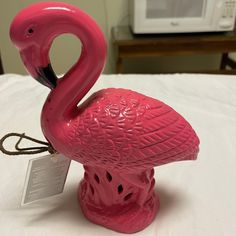 a pink flamingo figurine sitting on top of a white bed next to a microwave