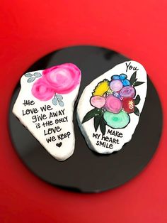 two decorated rocks sitting on top of a black plate with writing and flowers painted on them