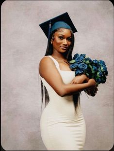 a woman wearing a graduation cap and gown holding blue roses in her hands while posing for the camera