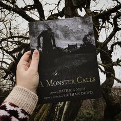 a person holding up a book in front of a tree with no leaves on it