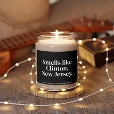 a candle that reads smells like clinton, new jersey next to a ukulele