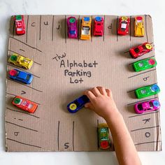 a child's hand writing on an alphabet parking lot with toy cars and trucks