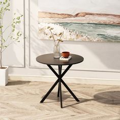 a small table with a vase on it in front of a painting and potted plant