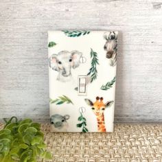 a white light switch cover with animals on it and green leaves around the lightshade