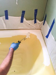 a man is painting the walls in a bathroom with yellow paint and blue adhesive tape