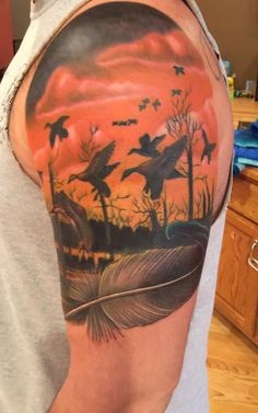 a man with a tattoo on his arm that has birds flying in the sky and trees