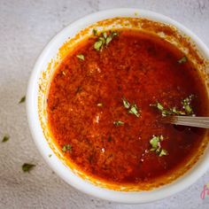 a white bowl filled with red sauce and garnished with parsley