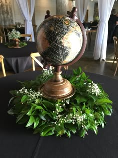 a globe on top of a table surrounded by greenery and white flowers in a banquet hall