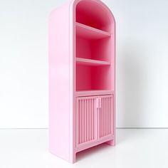 a pink shelf with an open door on the top and bottom section, in front of a white wall