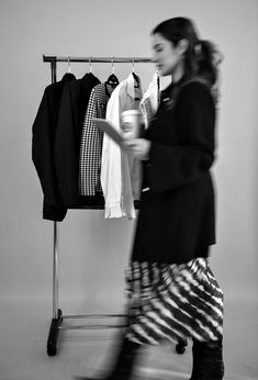 a woman walking past a rack with shirts hanging on it's hangers and holding a cup in her hand