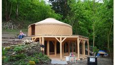 a yurt in the middle of a forest with people sitting on steps and around it