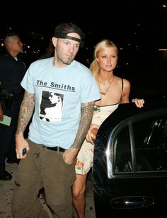 a man and woman standing next to each other in front of a car at night