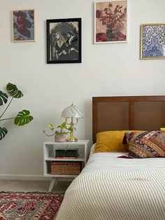 a bed sitting in a bedroom next to a wall with pictures on it and a potted plant