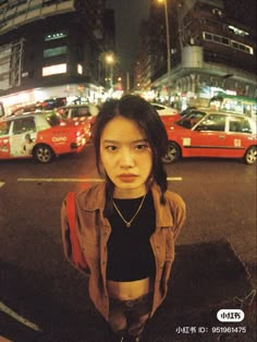 a woman standing in the middle of a street at night with cars parked on both sides