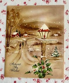 a christmas postcard with holly and mist on the snow covered ground in front of a snowy village